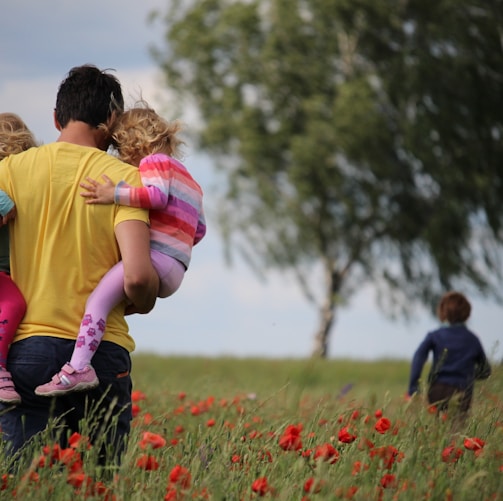 man carrying to girls on field of red petaled flower