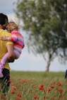 man carrying to girls on field of red petaled flower