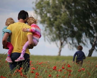 man carrying to girls on field of red petaled flower