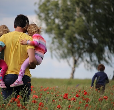 man carrying to girls on field of red petaled flower