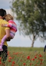 man carrying to girls on field of red petaled flower