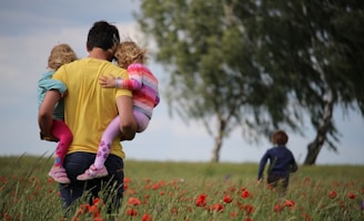 man carrying to girls on field of red petaled flower