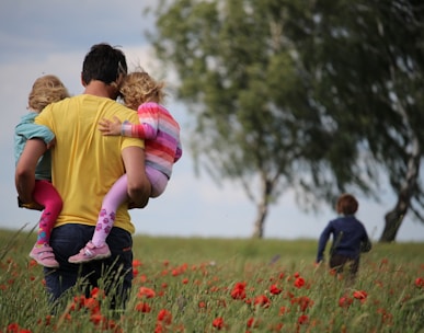 man carrying to girls on field of red petaled flower