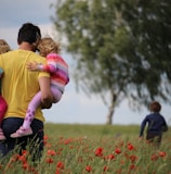 man carrying to girls on field of red petaled flower