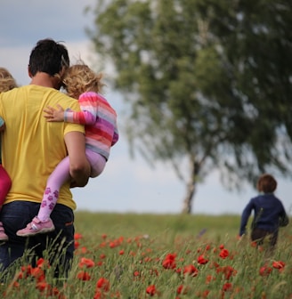 man carrying to girls on field of red petaled flower