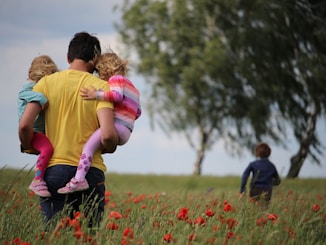 man carrying to girls on field of red petaled flower