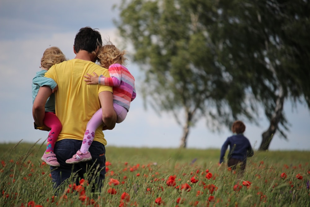 man carrying to girls on field of red petaled flower