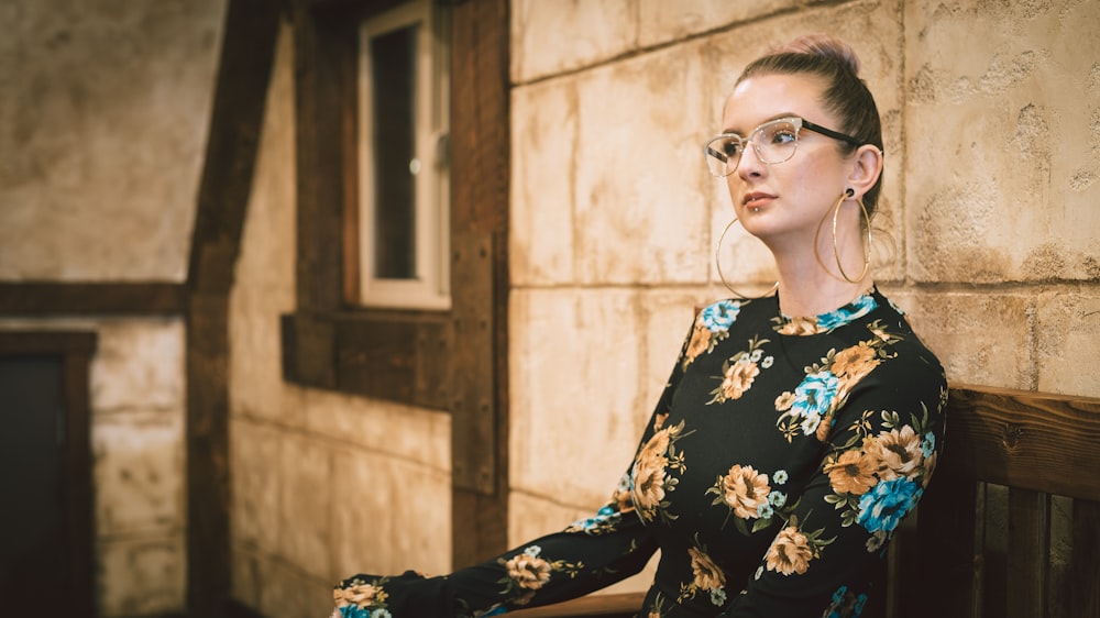 woman in black and multicolored floral long-sleeved top sitting on brown wooden chair beside beige wall