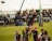 Rugby players are engaged in a line-out during a match, with one player being lifted high to catch the ball. The scene takes place on a grassy field surrounded by an audience, with branding and advertisements in the background.