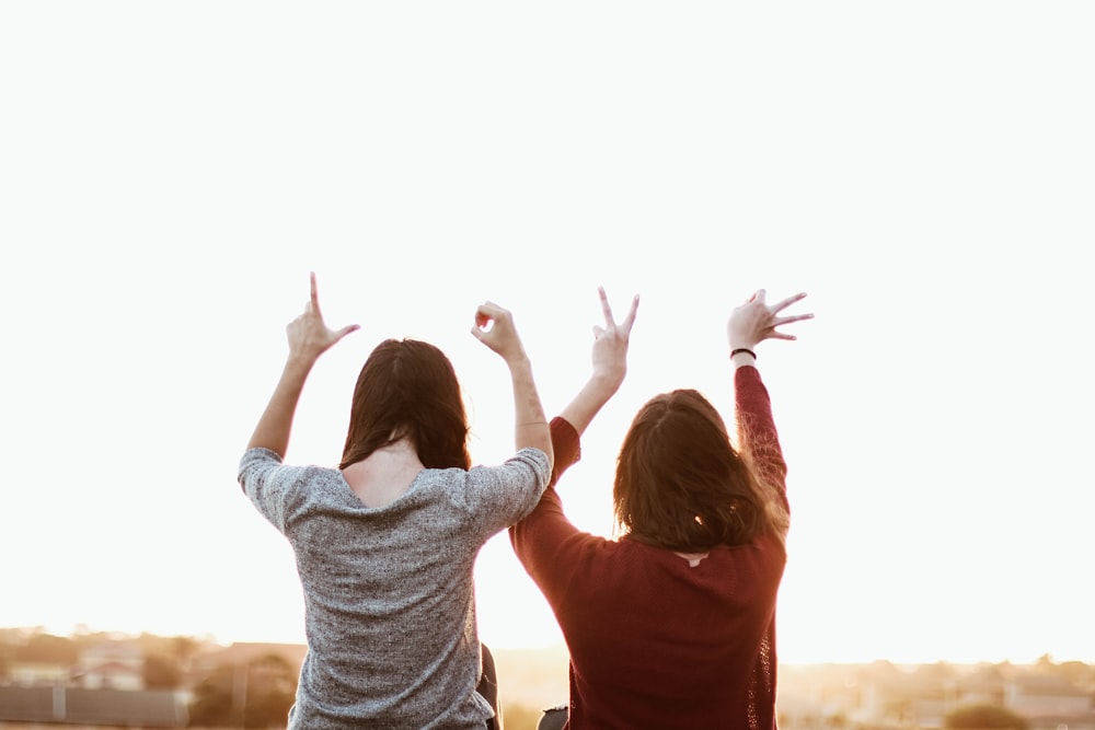 Dos mujeres sentadas mientras hacen el signo de la mano del amor durante el día