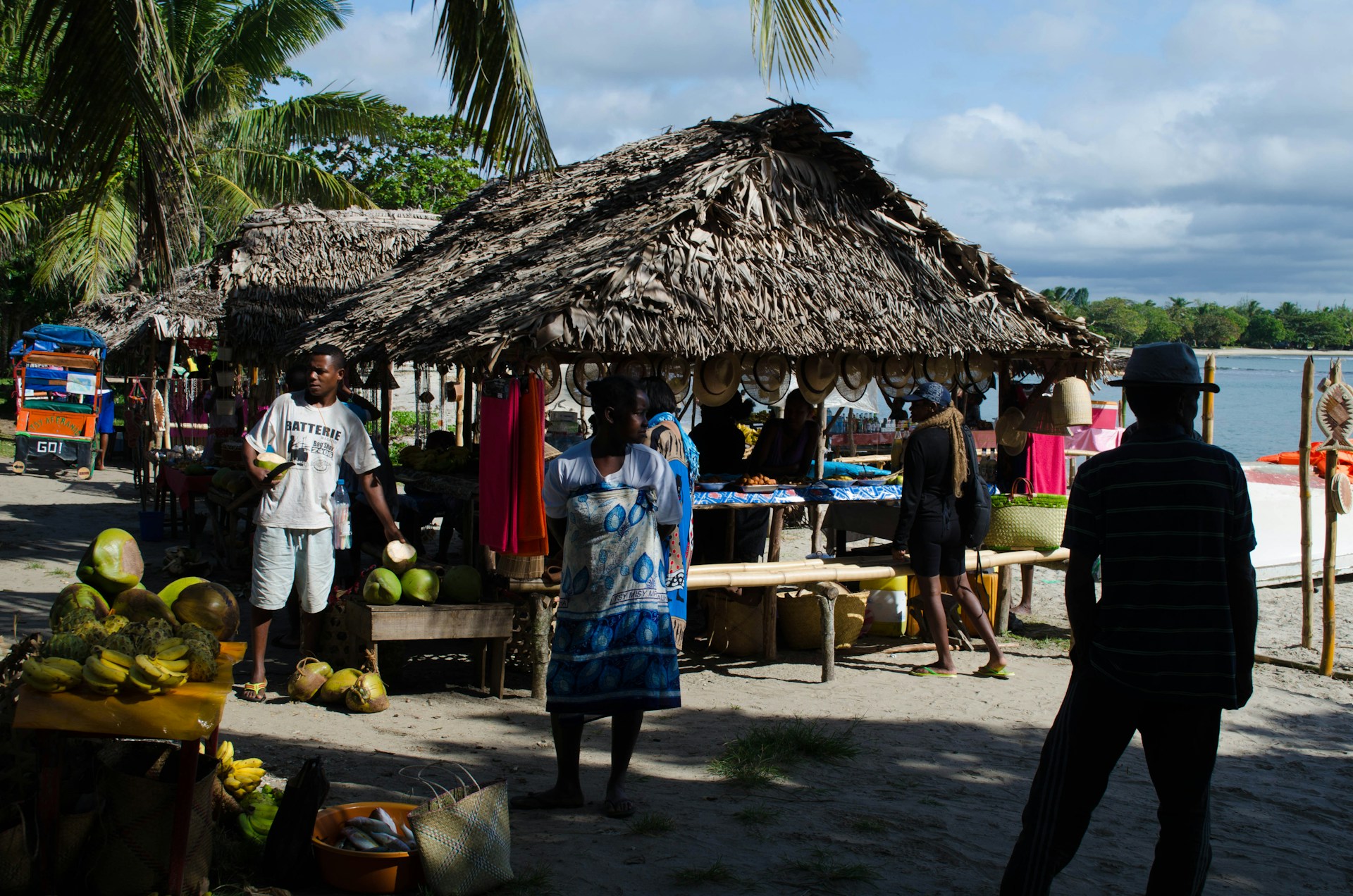 A bustling street market in a coastal town, filled with lively vendors and fresh local produce under bright awnings.