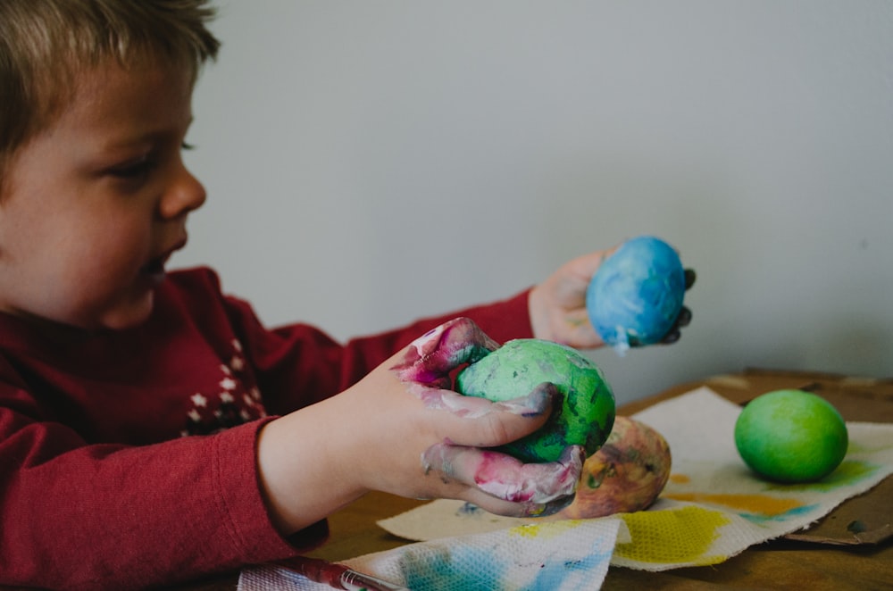 niño sosteniendo cáscaras de huevo pintadas de azul y verde
