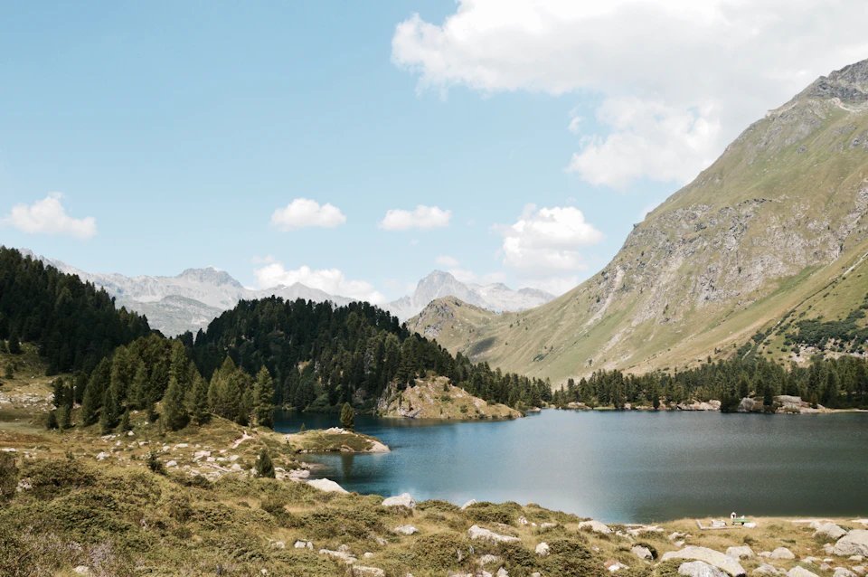Serene mountain lake surrounded by lush green mountains and trees reflects clear blue sky
