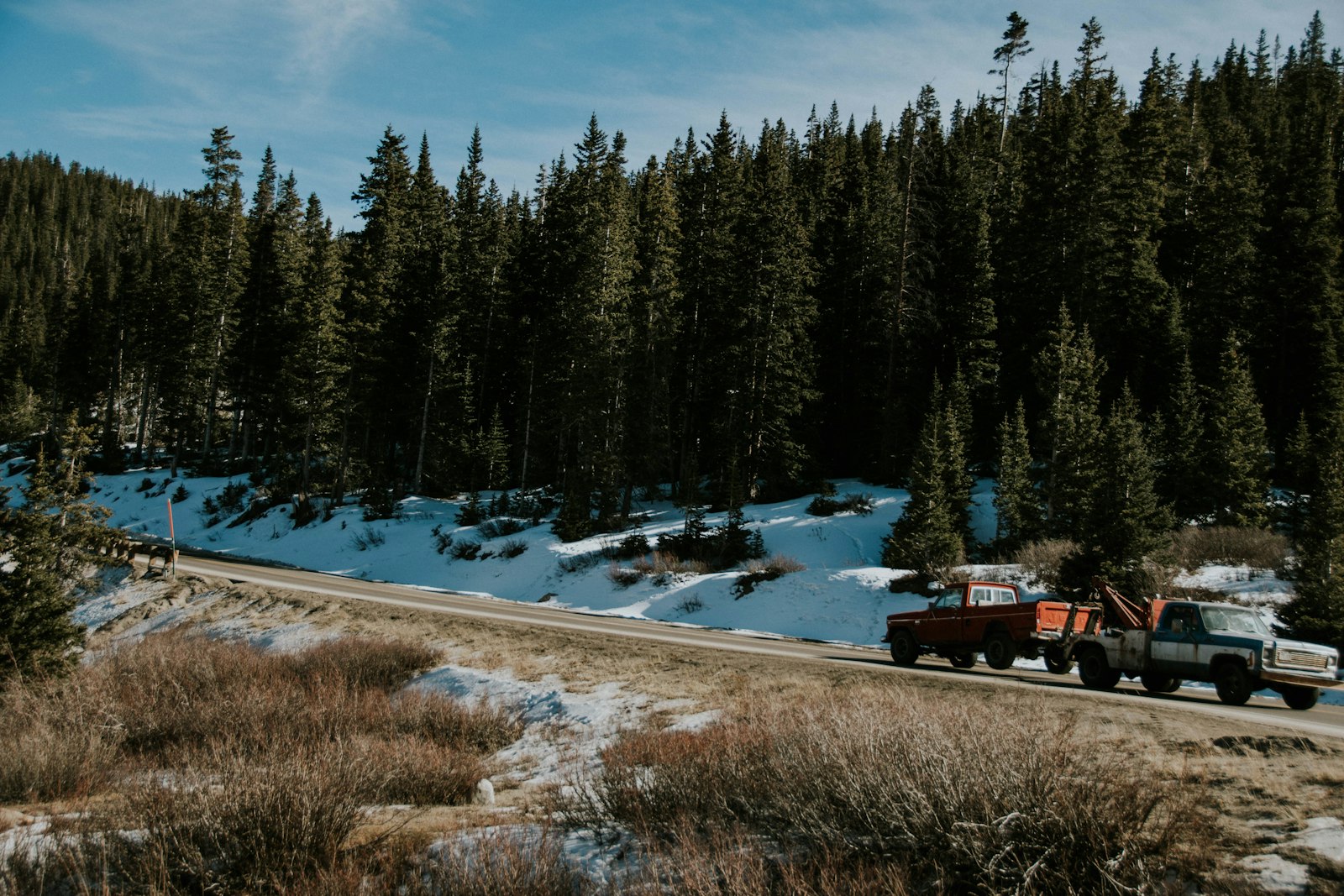 A tow truck hooked to a disabled vehicle on a sun-baked roadside shoulder.