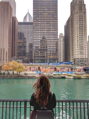 A professional portrait of Shididi standing by a flowing urban river, with city buildings in the background.