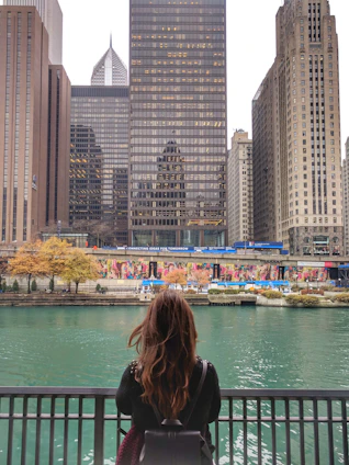 A professional portrait of Shididi standing by a flowing urban river, with city buildings in the background.