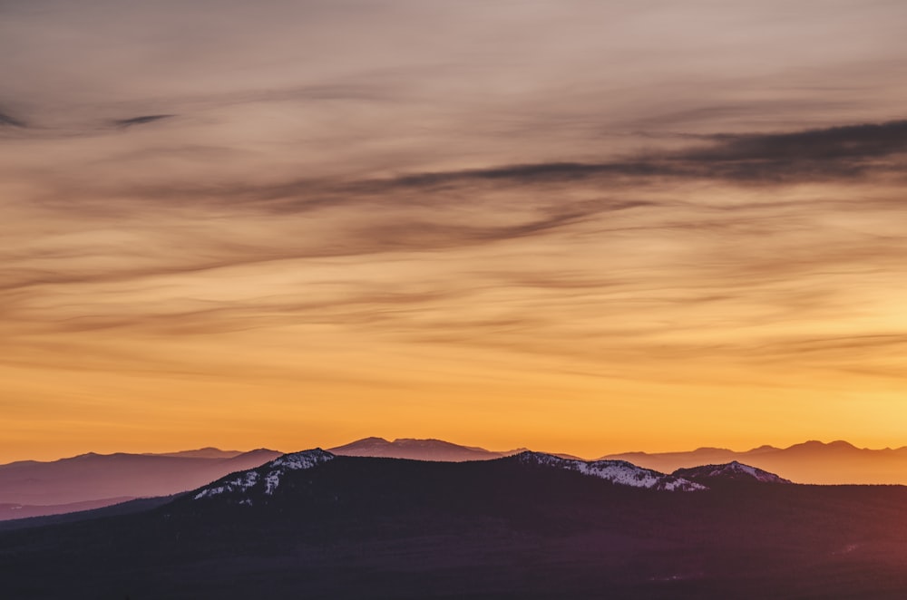 silhouette of mountain during yellow cloudy skies