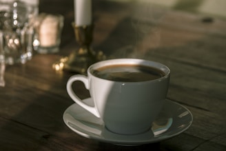 A steaming cup of herbal coffee beside a small bowl of natural capsules on a wooden table, with soft morning light.