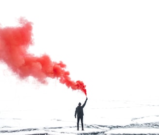 selective color photography of person holding orange gas smoke standing on snow
