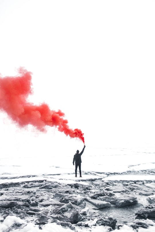 selective color photography of person holding orange gas smoke standing on snow in Oeschinen Lake Switzerland