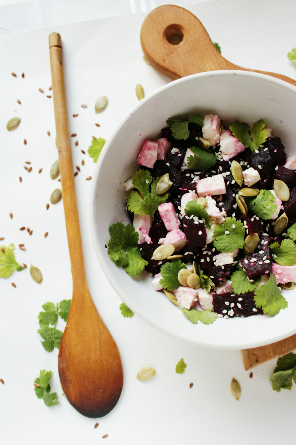 vegetable salad topped with sesame seeds in round white ceramic bowl beside brown wooden ladle