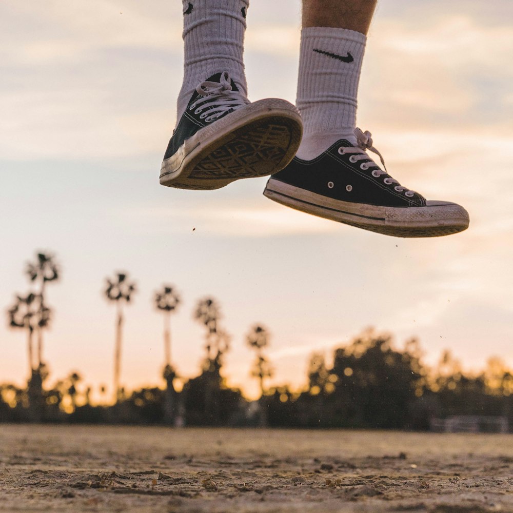 person wearing black low-top sneakers jumping high under white sky