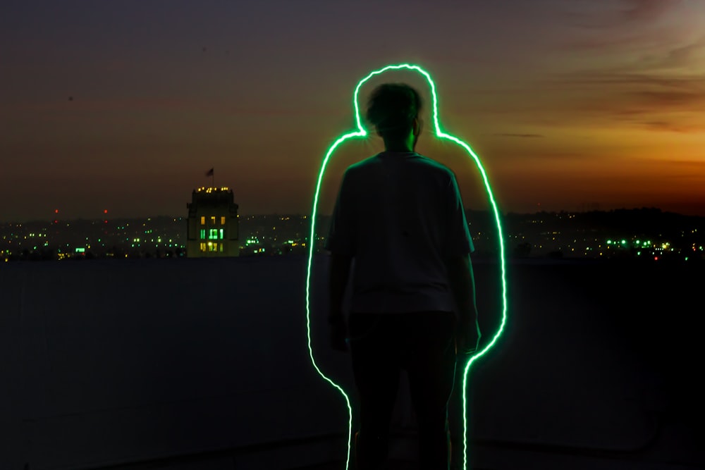 silhouette of man standing with green neon outline during sunset