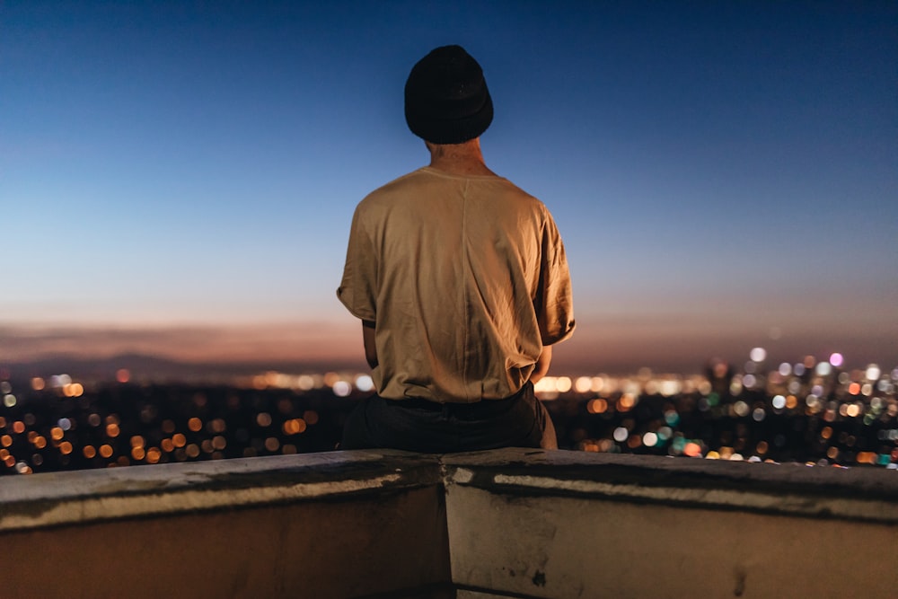 person sitting on rooftop ledge during nighttime