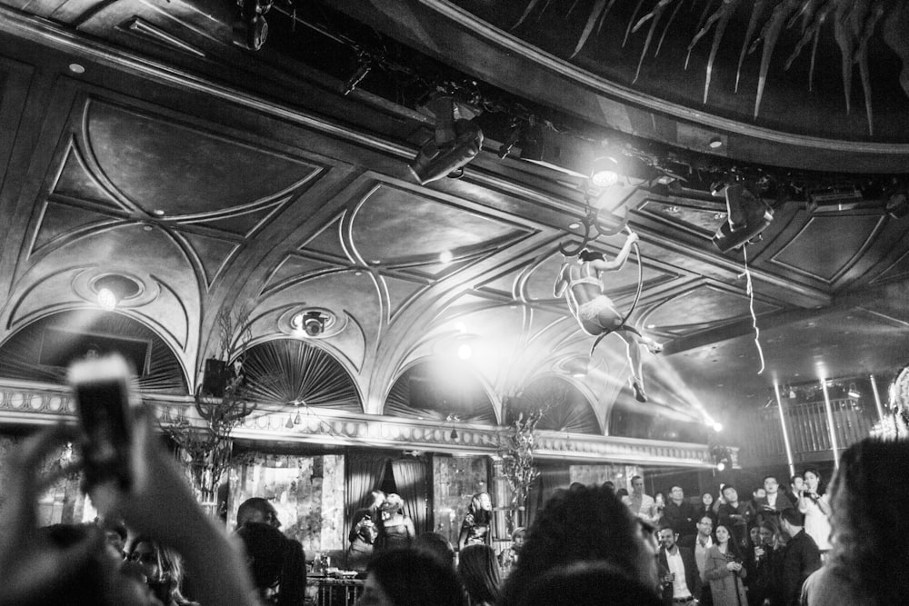 grayscale photography of woman hanging near ceiling surrounded by crowd
