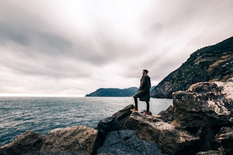 man standing on boulder near body of water