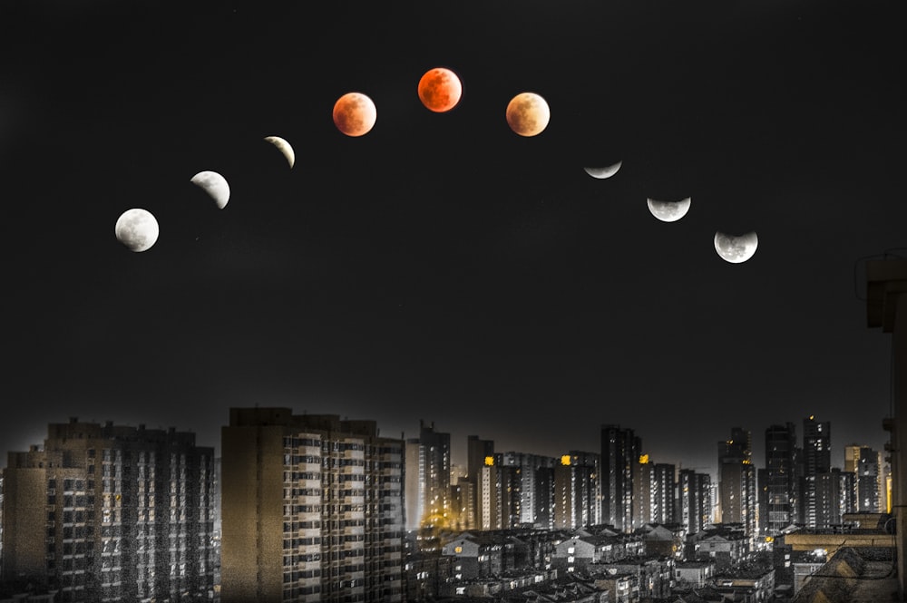 white and red moon over lighted high-rise buildings during night time