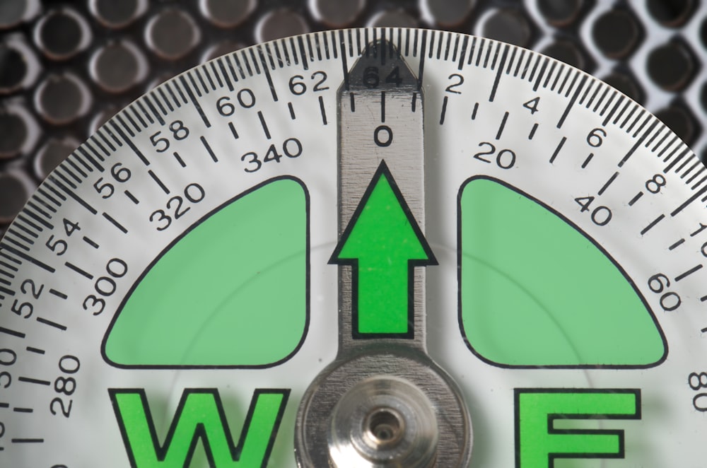 a close up of a compass with a green arrow