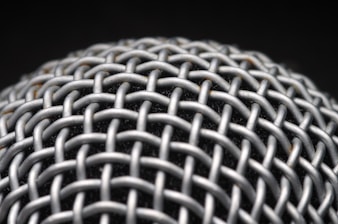 A close-up view of a metallic mesh structure with a grid-like pattern. The material appears to be interwoven, creating a textured and intricate design. The background is dark, highlighting the metallic surface.