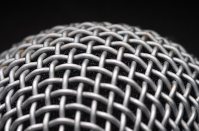 A close-up view of a metallic mesh structure with a grid-like pattern. The material appears to be interwoven, creating a textured and intricate design. The background is dark, highlighting the metallic surface.
