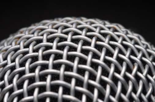 A close-up view of a metallic mesh structure with a grid-like pattern. The material appears to be interwoven, creating a textured and intricate design. The background is dark, highlighting the metallic surface.