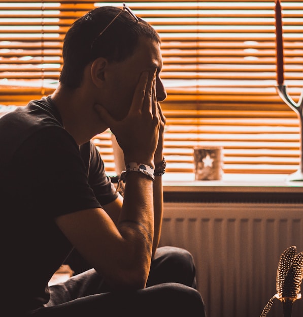 man sitting on chair covering his eyes