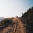 A rugged off-road vehicle travels along a dusty, unpaved path bordered by wild vegetation. The scene conveys a sense of adventure and remoteness under a clear blue sky.