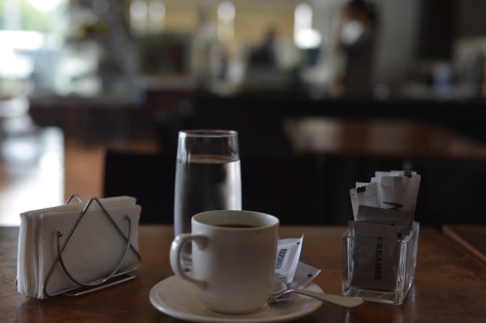 selective focus photography of teacup beside tissue and drinking glass on top of table