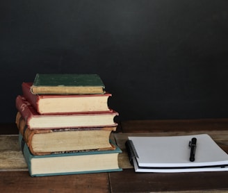 pile of books beside white printer paper and black ballpoint pen