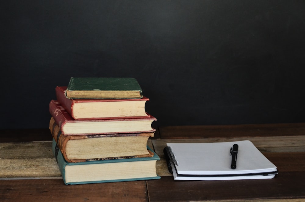 흰색 프린터 용지와 검은색 볼펜 옆에 있는 책 더미