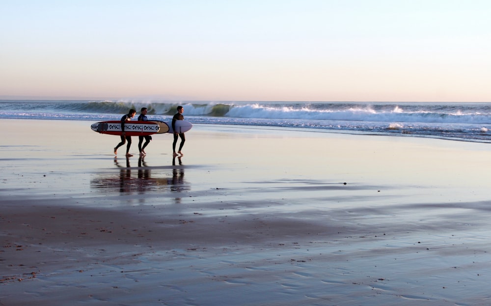 three man holding surfboard while walking on seashore