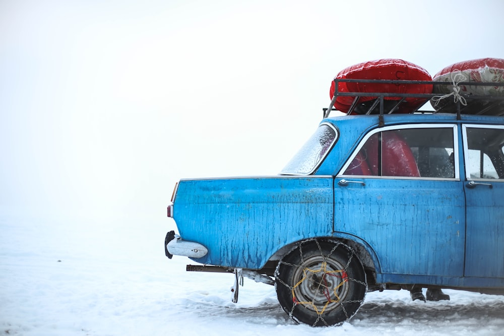 sedán azul con cadena en el neumático estacionado en un campo de nieve durante el día