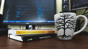 A creative workspace with AI-related books, code on a monitor, and a cup of coffee.