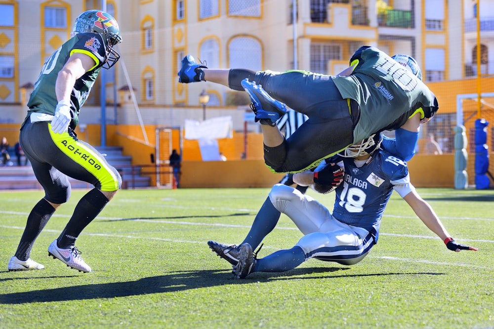 football player in green jersey tackling player in blue jersey