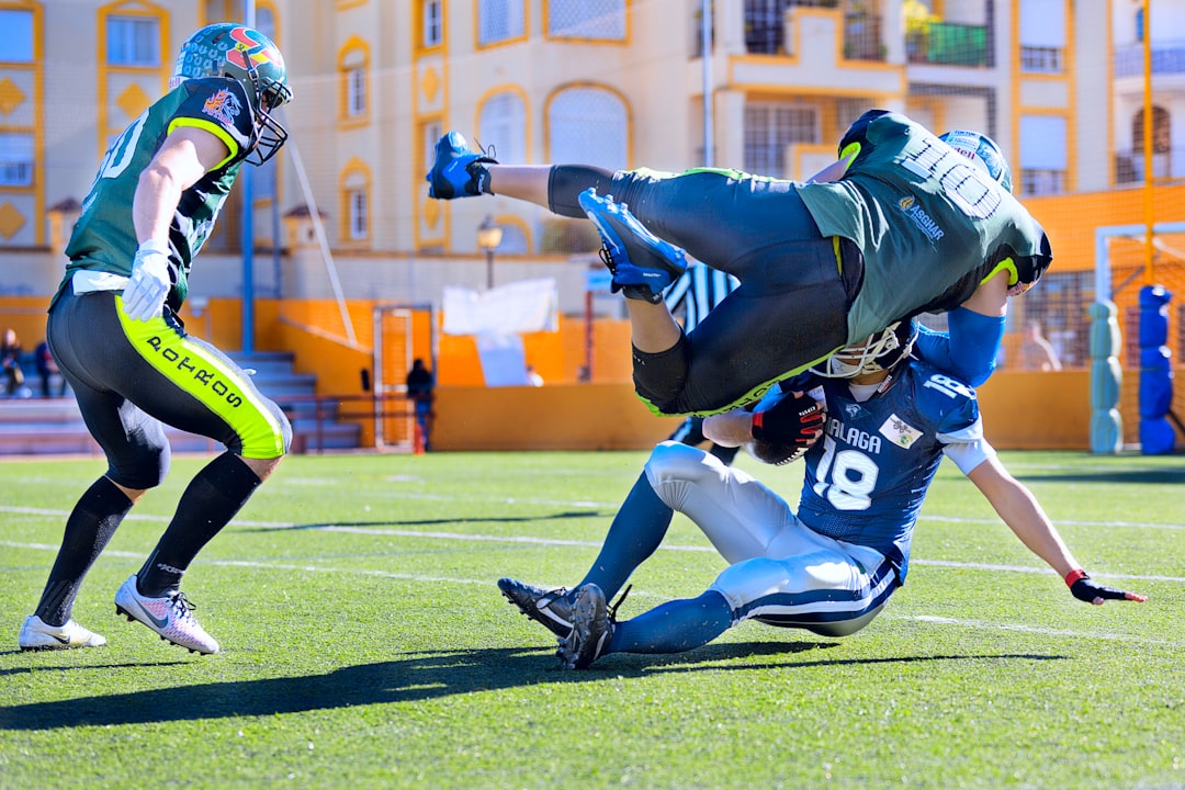 football player in green jersey tackling player in blue jersey