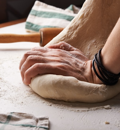 person making dough beside brown wooden rolling pin