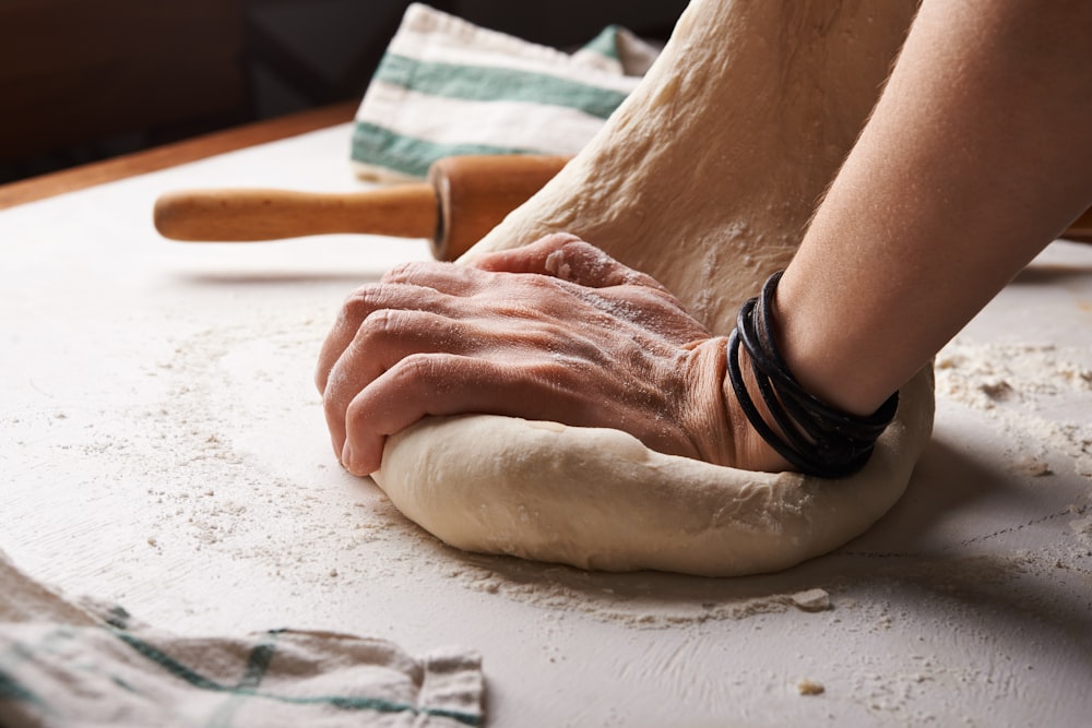 personne faisant de la pâte à côté d’un rouleau à pâtisserie en bois brun