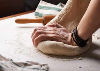 person making dough beside brown wooden rolling pin