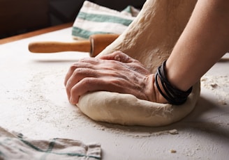 person making dough beside brown wooden rolling pin