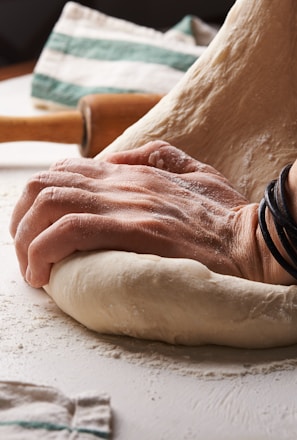 person making dough beside brown wooden rolling pin